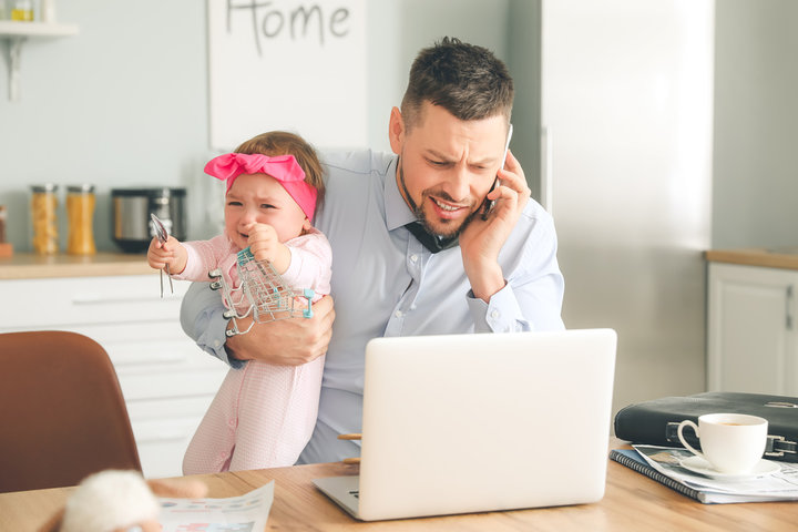 Man works from home with a baby in his arms and phone in other hand